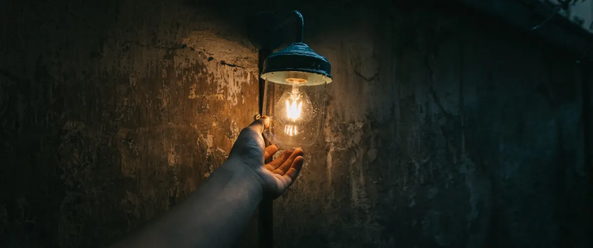 A person checking a lit bulb inside a covered lamp
